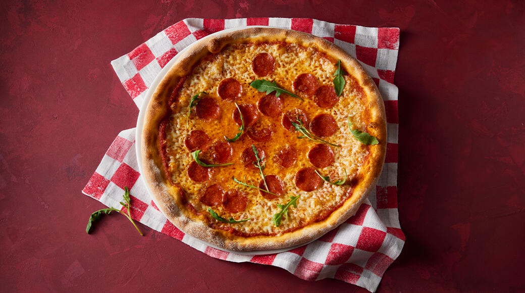 Pepperoni pizza topped with rocket leaves on a red and white checkered cloth on a red table.