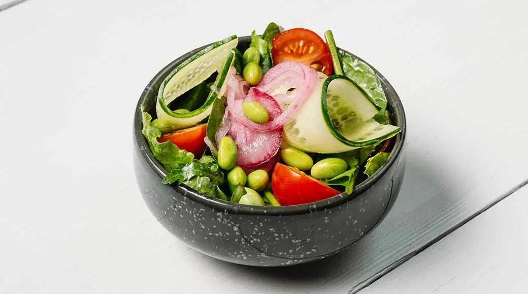 Värske salat tumedas kausis kurgilintide, tomati, edamame ubade, punase sibula ja lehtsalatiga.
