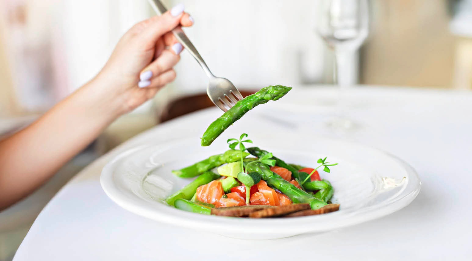 Kahvel tõstmas sparglit valge taldrikult, millel on lõhe, spargli ja avokaadoga toit.