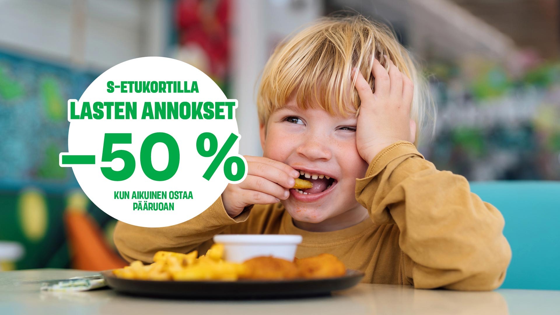 Lapsi hymyilee syödessään ruokaa ravintolassa, edessään annos ranskalaisia perunoita ja nugetteja.