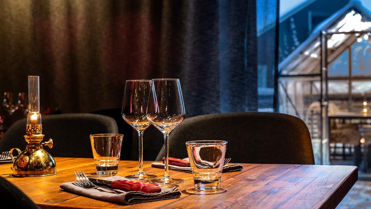 Asiakkaille valmiiksi katettu pöytä aterimilla, vesilaseilla ja viinilaseilla.
