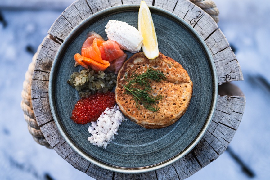 Lautasella oleva perinteinen suomalainen blini, jossa päällä tilliä, sekä sivuilla mätiä, sipulihackia, smetanaa, sitruunaa ja lohta.