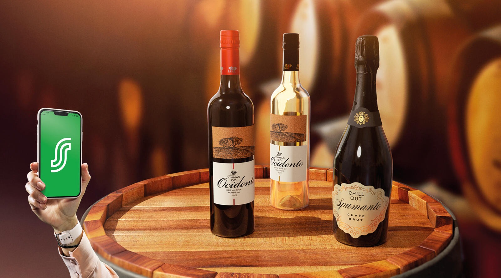 Tre vinflaskor på ett träfat och en hand som håller en smarttelefon med en grön app på skärmen.