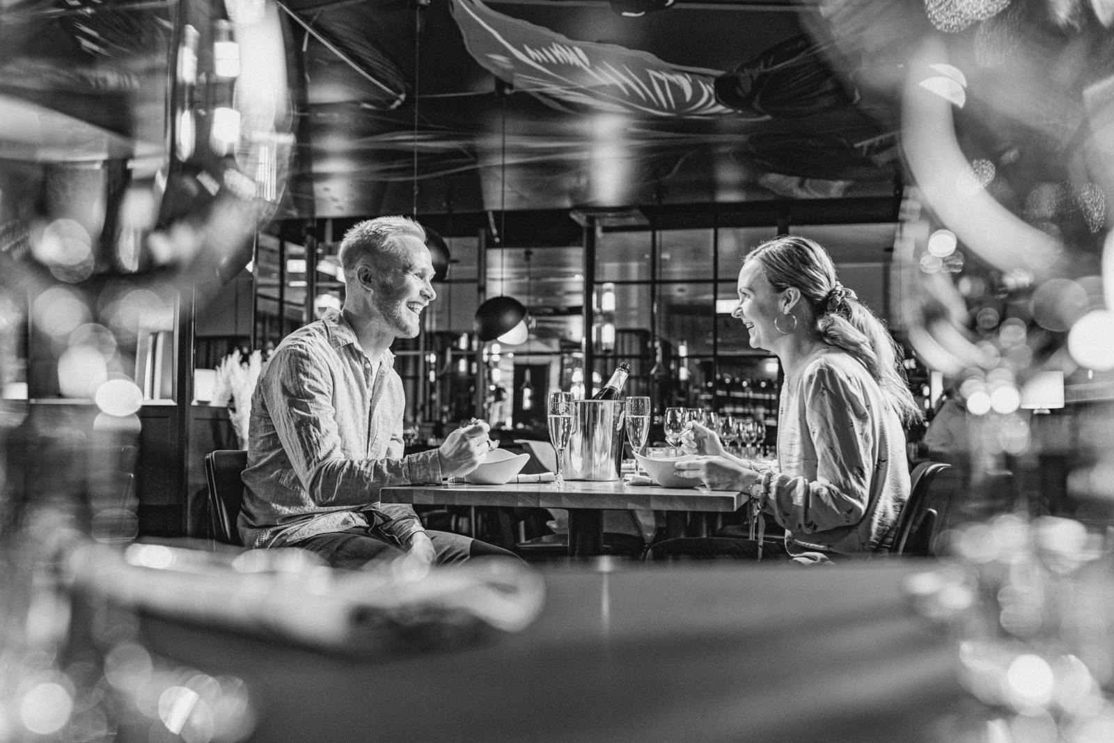 Kaks inimest nautimas õhtusööki restorani lauas. Laual on šampanjapudel jääämbrises ja klaasid.