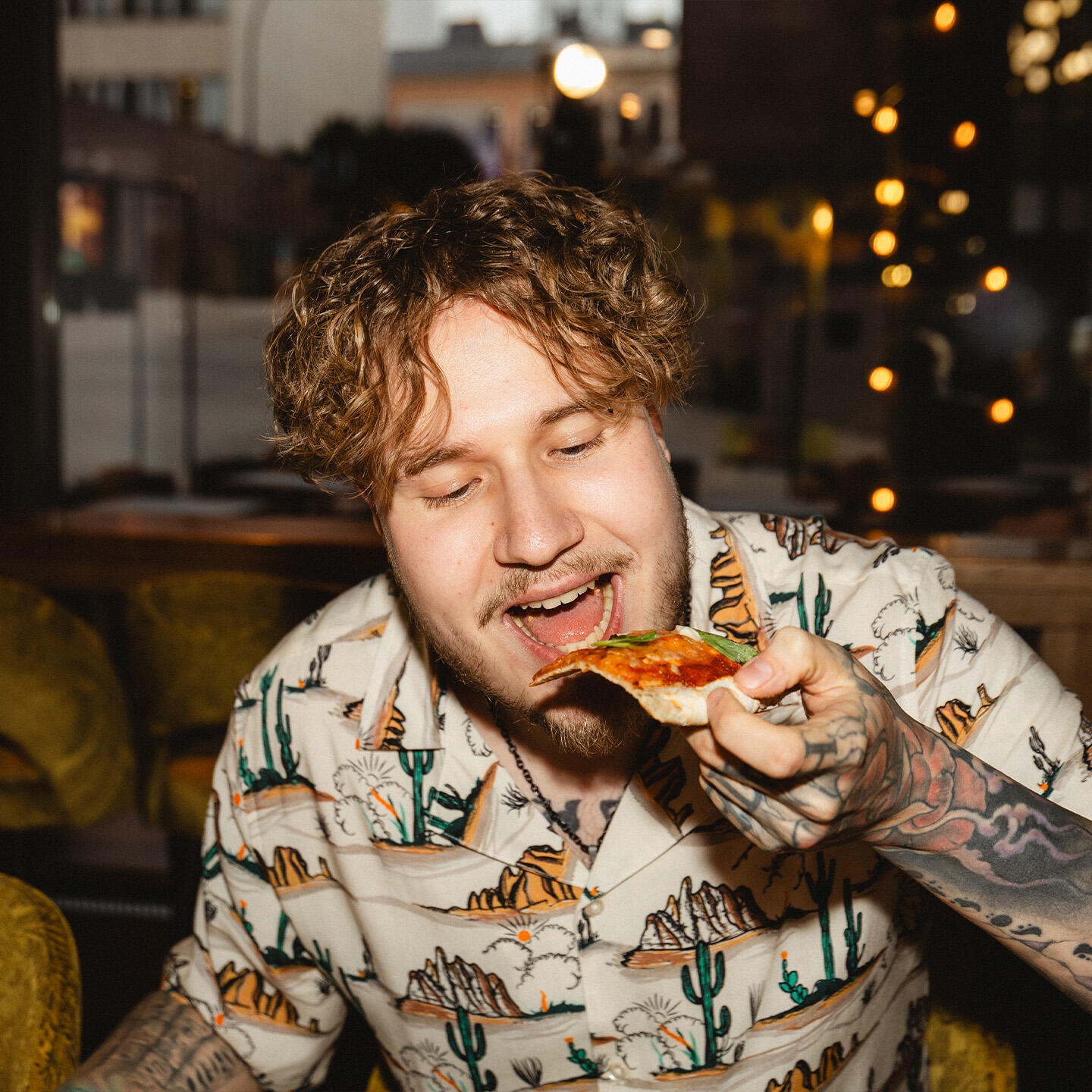 Henkilö syö pizzapalaa ravintolassa, jossa taustalla näkyy koristevaloja.