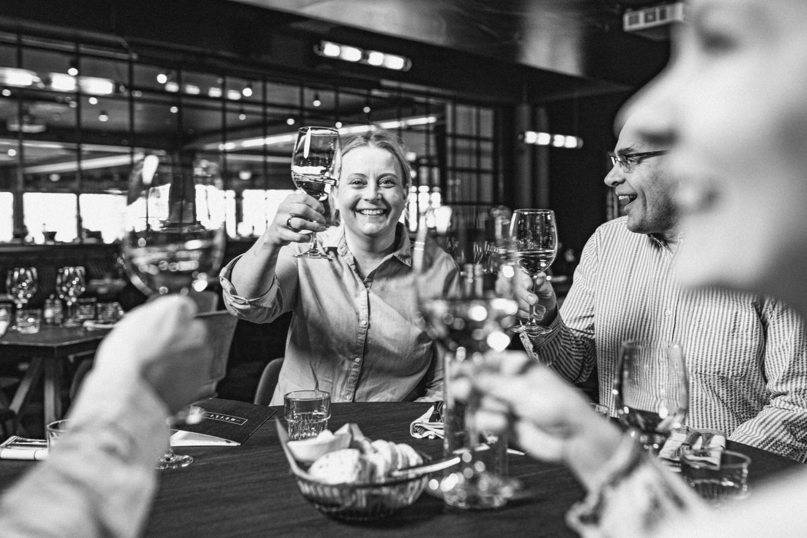 Inimesed tõstavad restoranis veiniklaase, tähistades meeleolukalt. Laual on näha leivakorv.