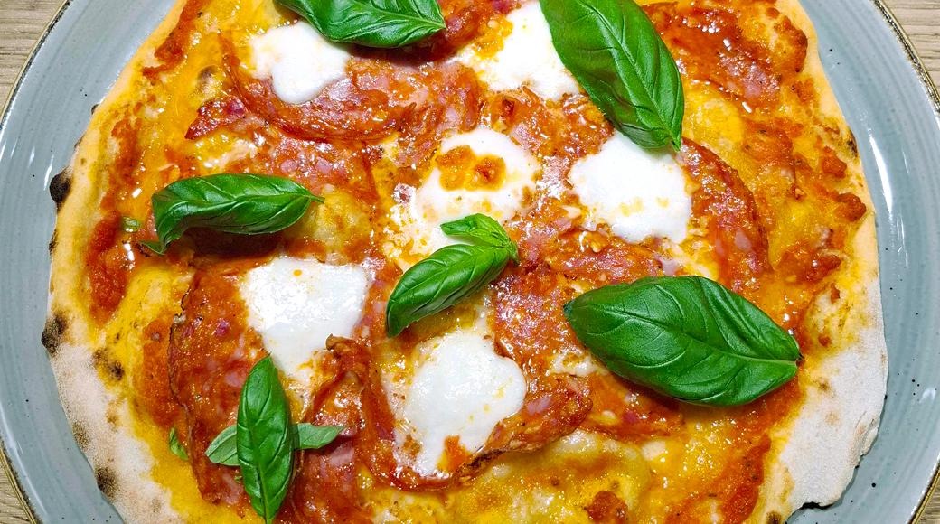Salamipizza, jossa on tomaattikastiketta, mozzarellajuustoa ja tuoreita basilikanlehtiä harmaalla lautasella.