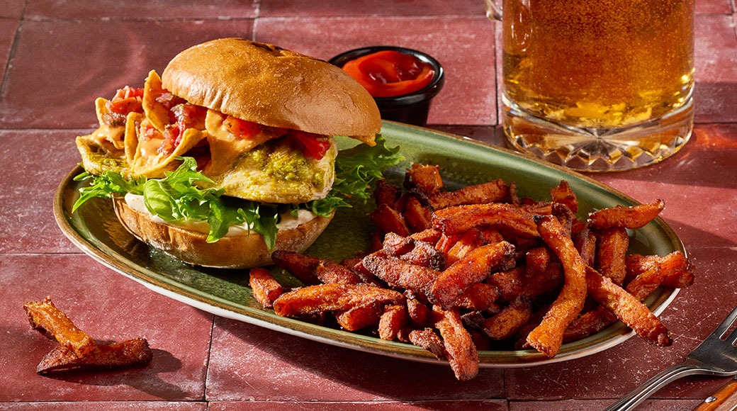 Mexicanburgeri salaatilla ja tomaattisalsalla sekä bataattiranskalaisia vihreällä lautasella. Vieressä lasillinen olutta ja dippikuppi.