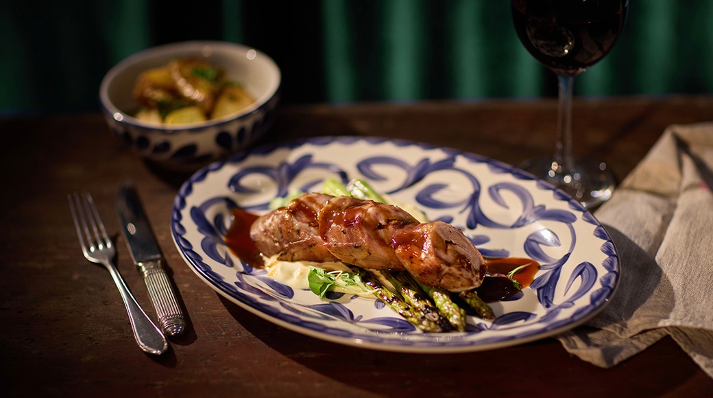 Praetud liharull kartulipüree ja spargliga sinisel-valgel mustrilise taldrikul. Taustal kauss ja veiniklaas.