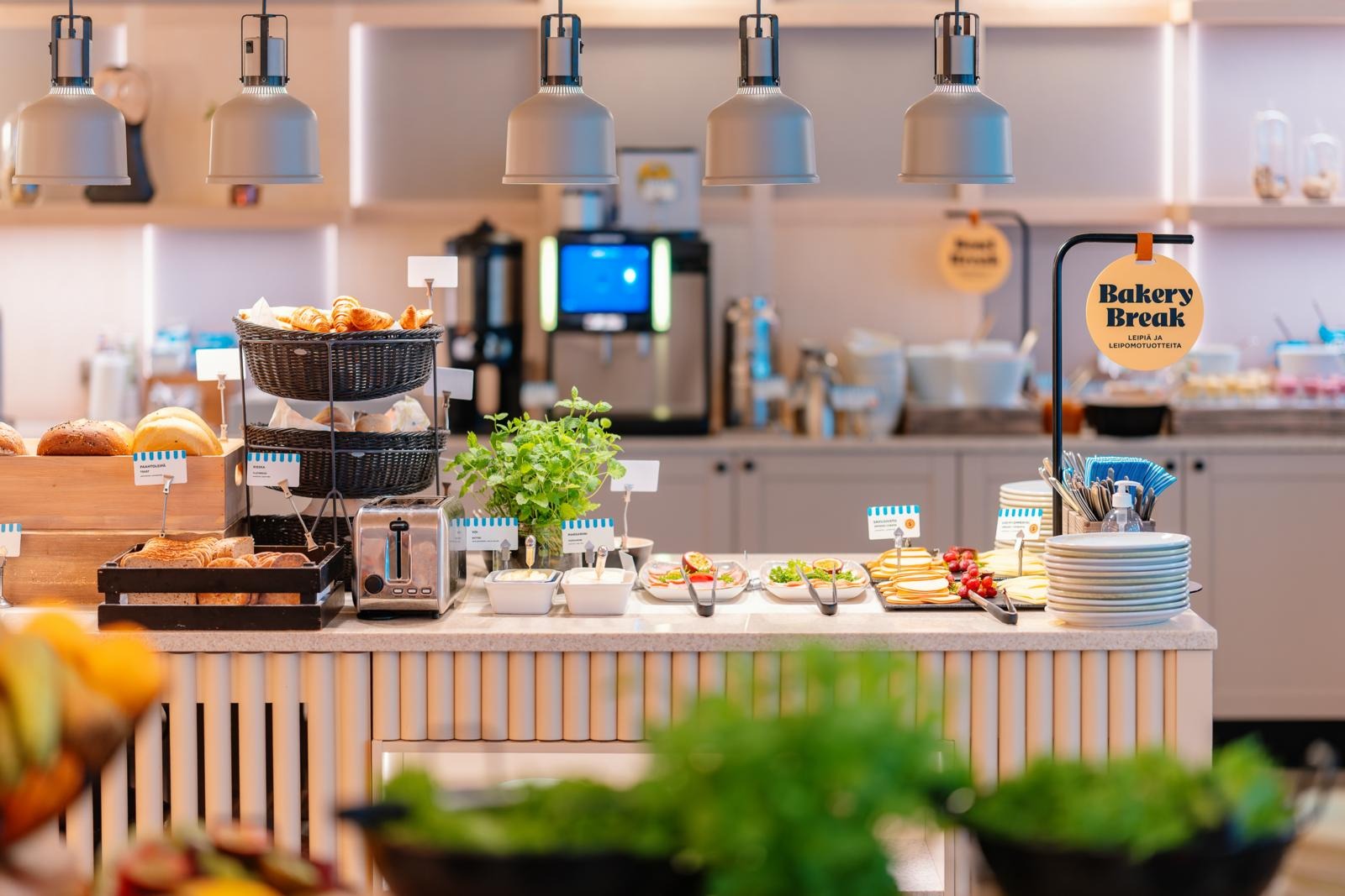 Tuoreita leipiä ja leikkeleitä tarjolla ravintola Kiisan aamiaisella. Etualalla hedelmiä ja kasviksia, takana kahvia.