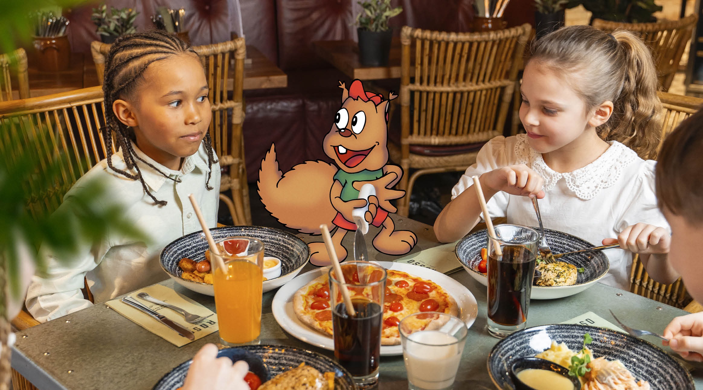 Kaksi lasta ravintolassa ruokailemassa, pöydällä pizza ja juomia. Keskellä animoitu orava-hahmo.