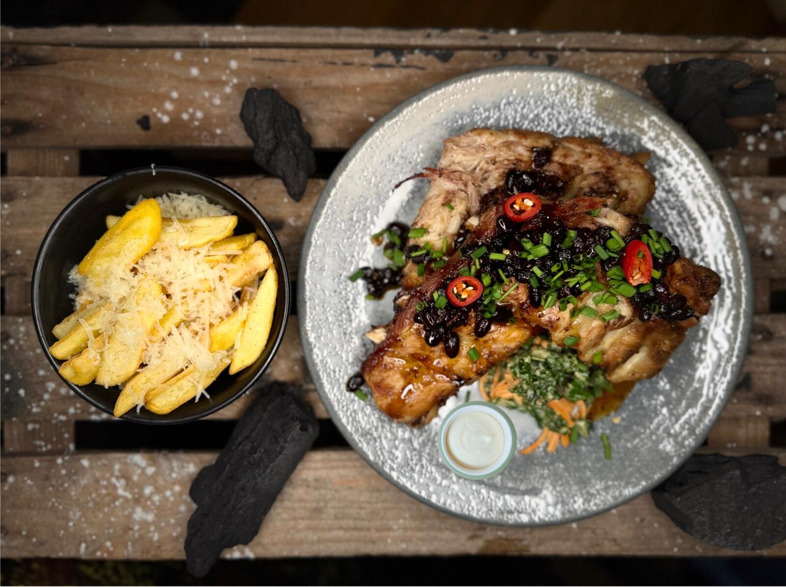 Plate of roasted meat with cherry sauce, green onions and chili peppers, alongside cheesy french fries.