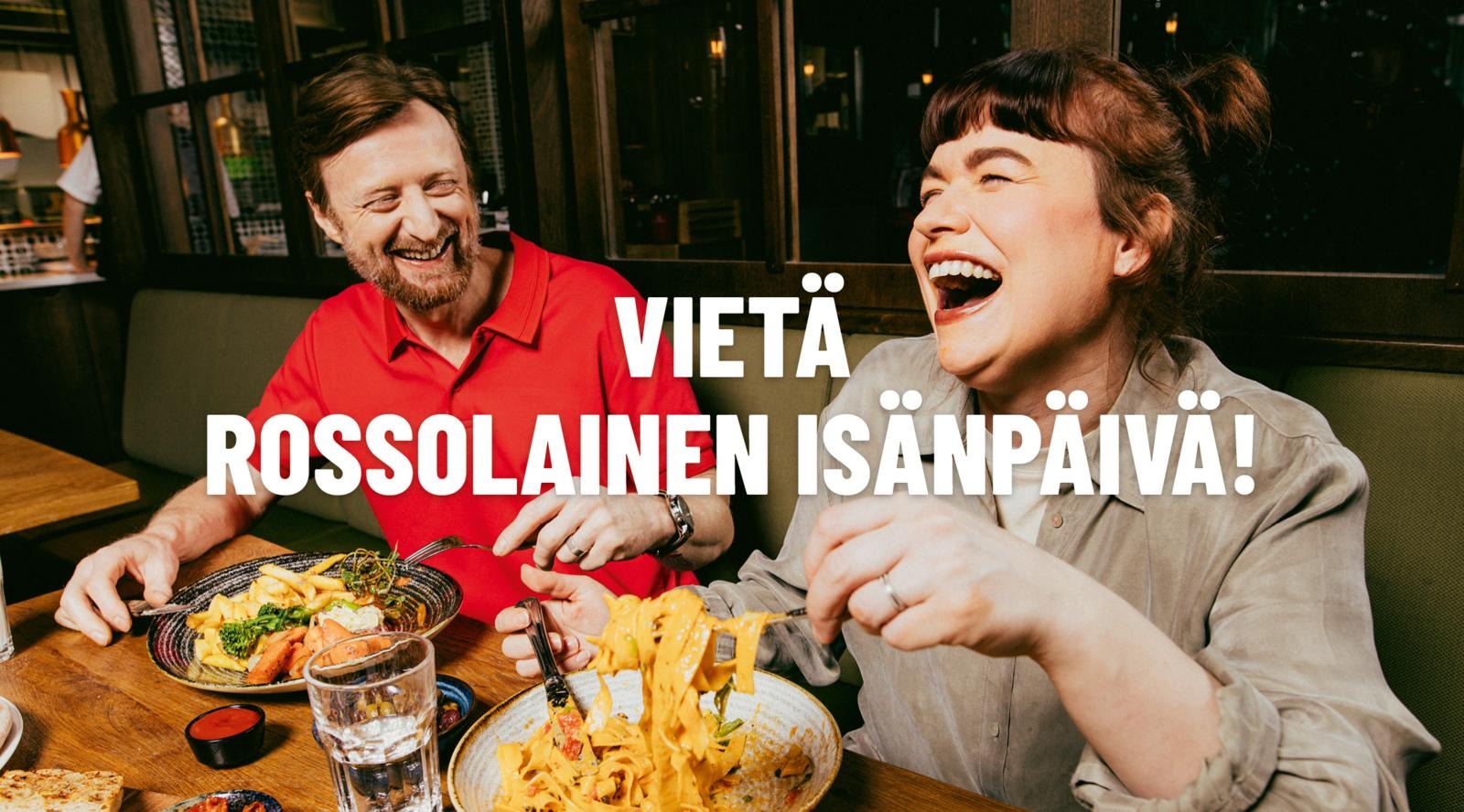 Kaks inimest naudivad oma einet restoranis, üks punases särgis ja teine beeži särgis, mõlemad naermas südamlikult, süües puulaual.