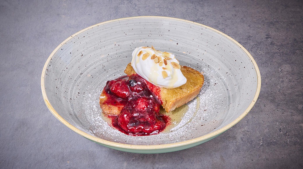 Köyhät ritarit kermavaahdon ja marjakastikkeen kanssa keraamisella lautasella.