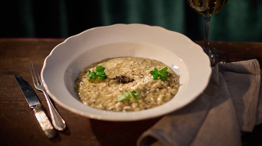 Taldrik seenerisotoga, kaunistatud peterselliga, kõrval veiniklaas ja söögiriistad puulaual.