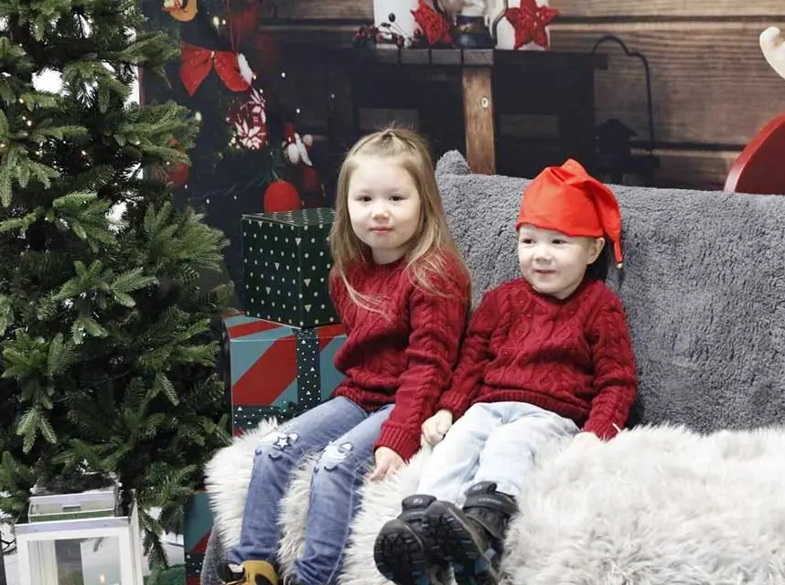 Kaksi lasta istuu joulukuusen vieressä sohvalla