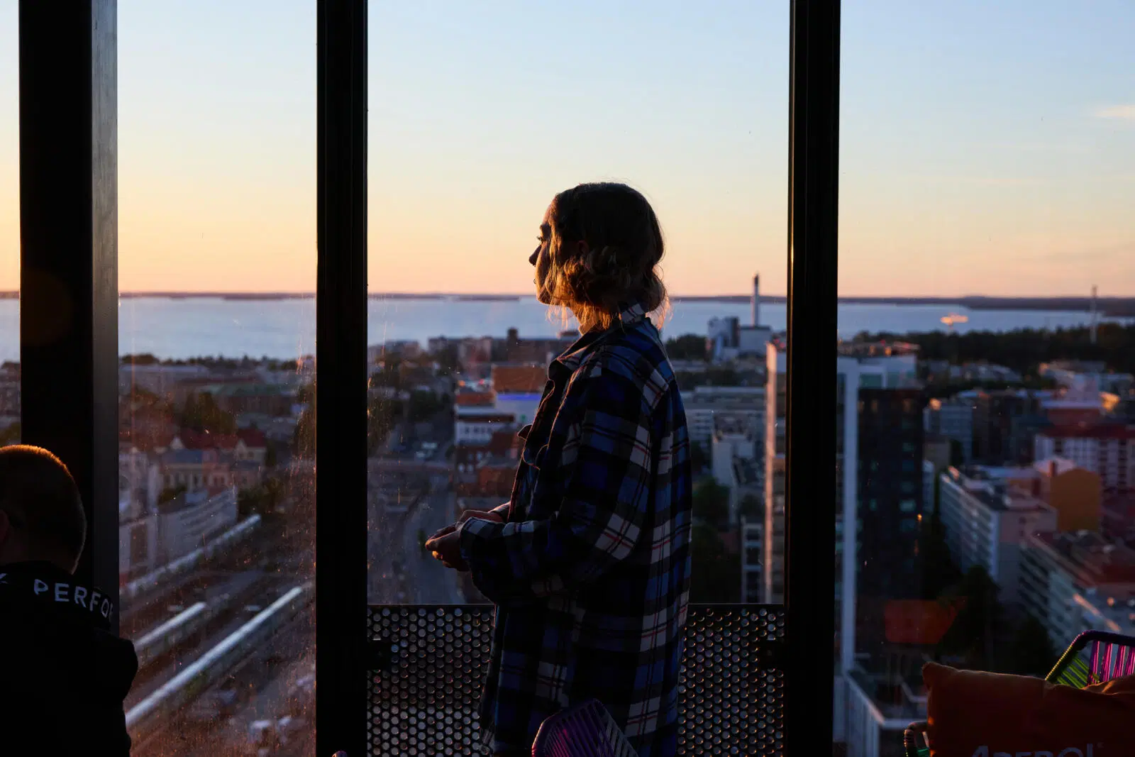 Nainen katsoo iltamaisemaa kattobaarin ikkunasta.