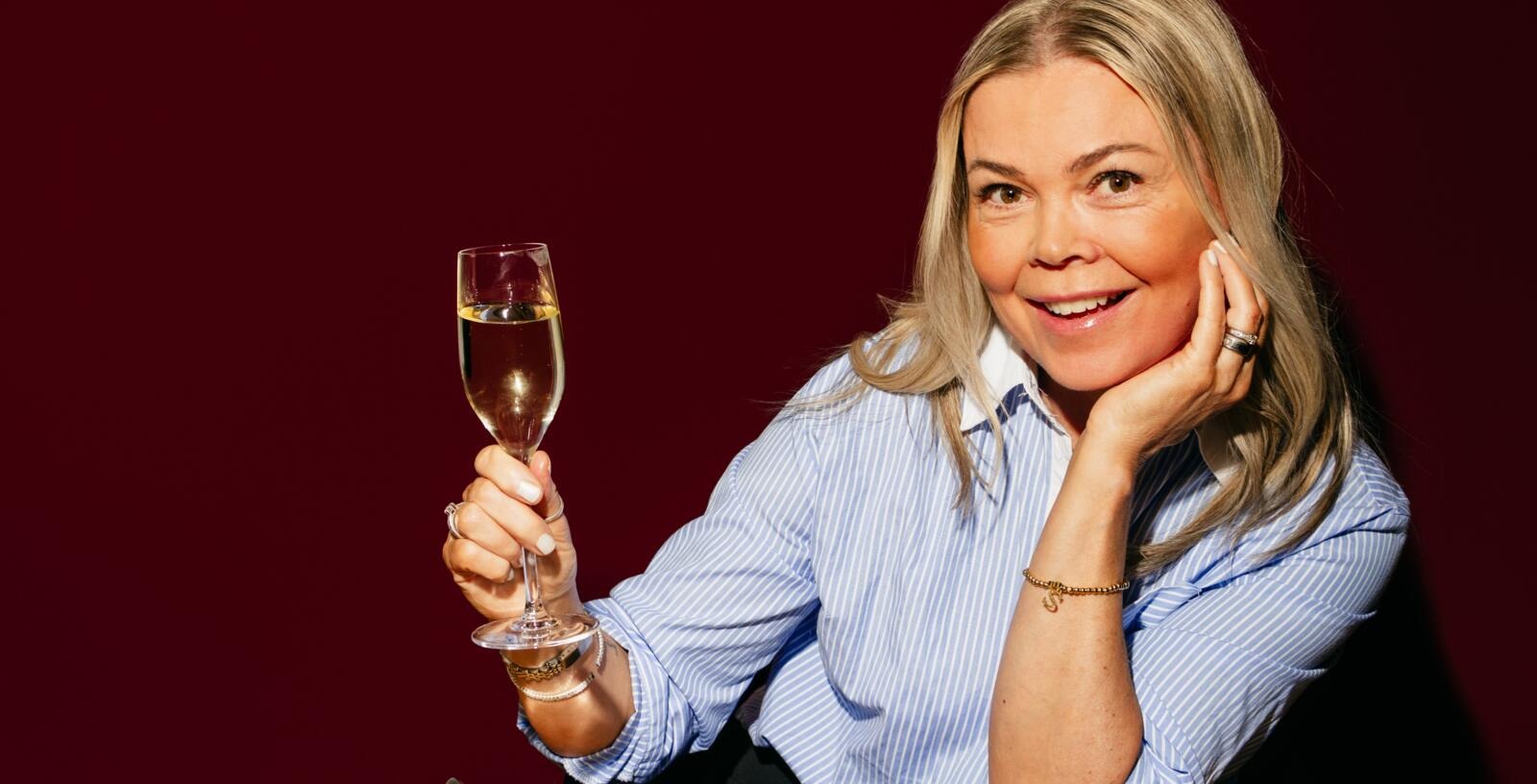 Nainen kohottaa kuohuviinilasia ravintolassa ja hymyilee