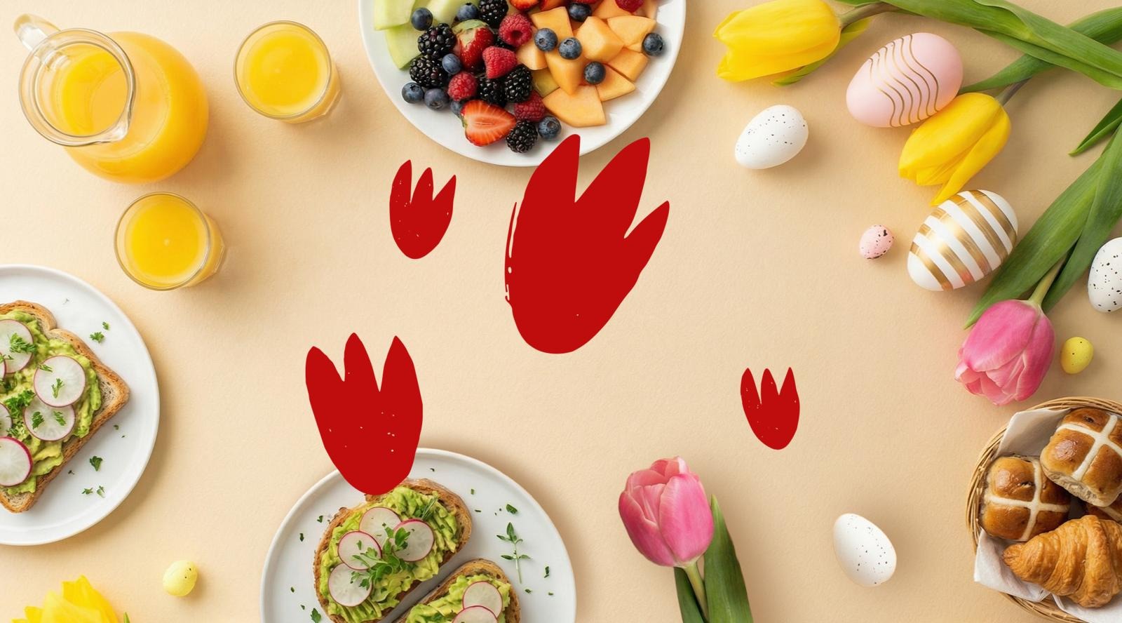 Pääsiäisaamiainen pöydällä: hedelmäsalaattia, avokadoleipää, mehuja, tulppaaneja, koristekananmunia ja pullia punaisilla kukkakuvioilla.