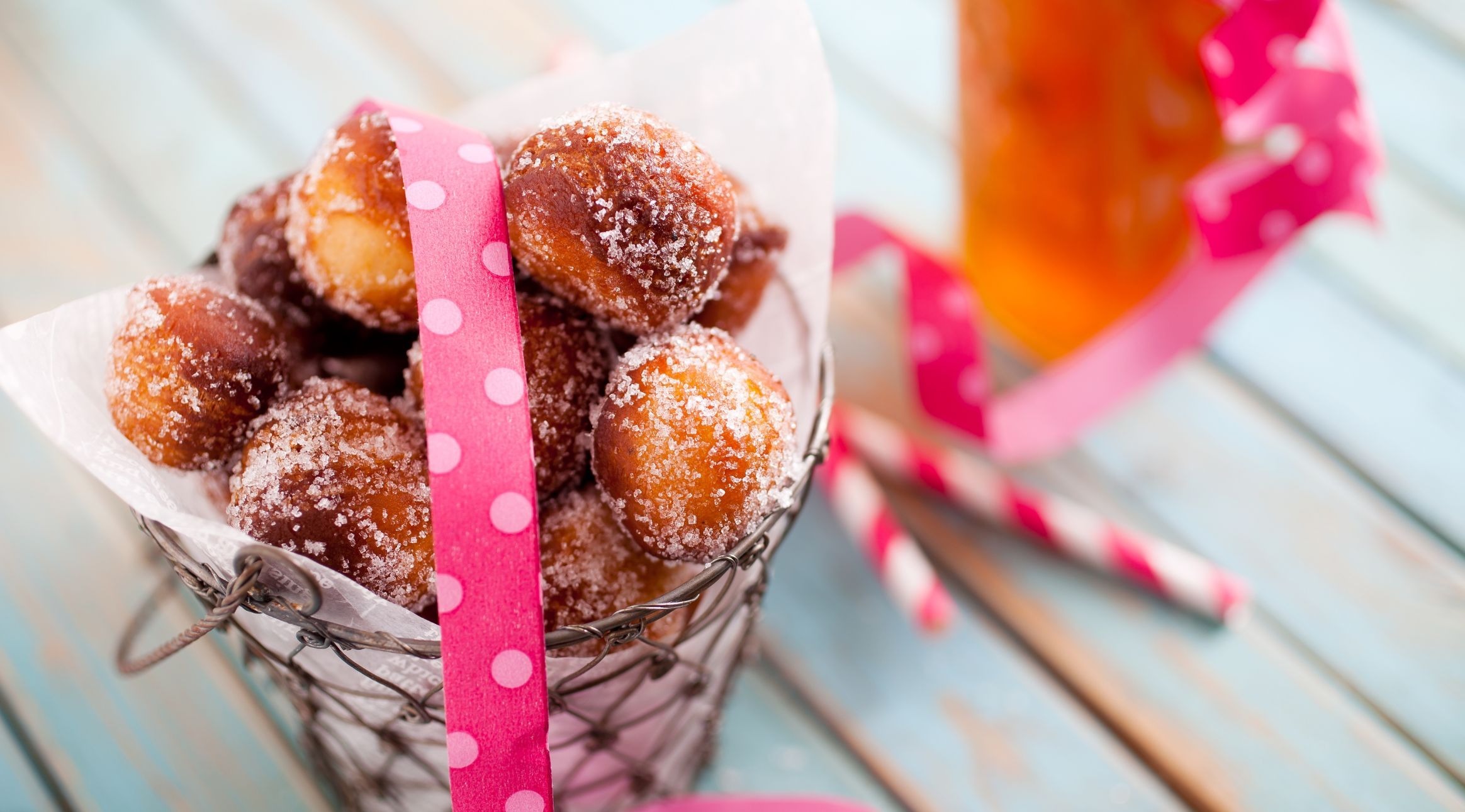 Suhkruga kaetud sõõrikupallid metallkorvis roosa täpiline lindiga helesinisel puitlaual.