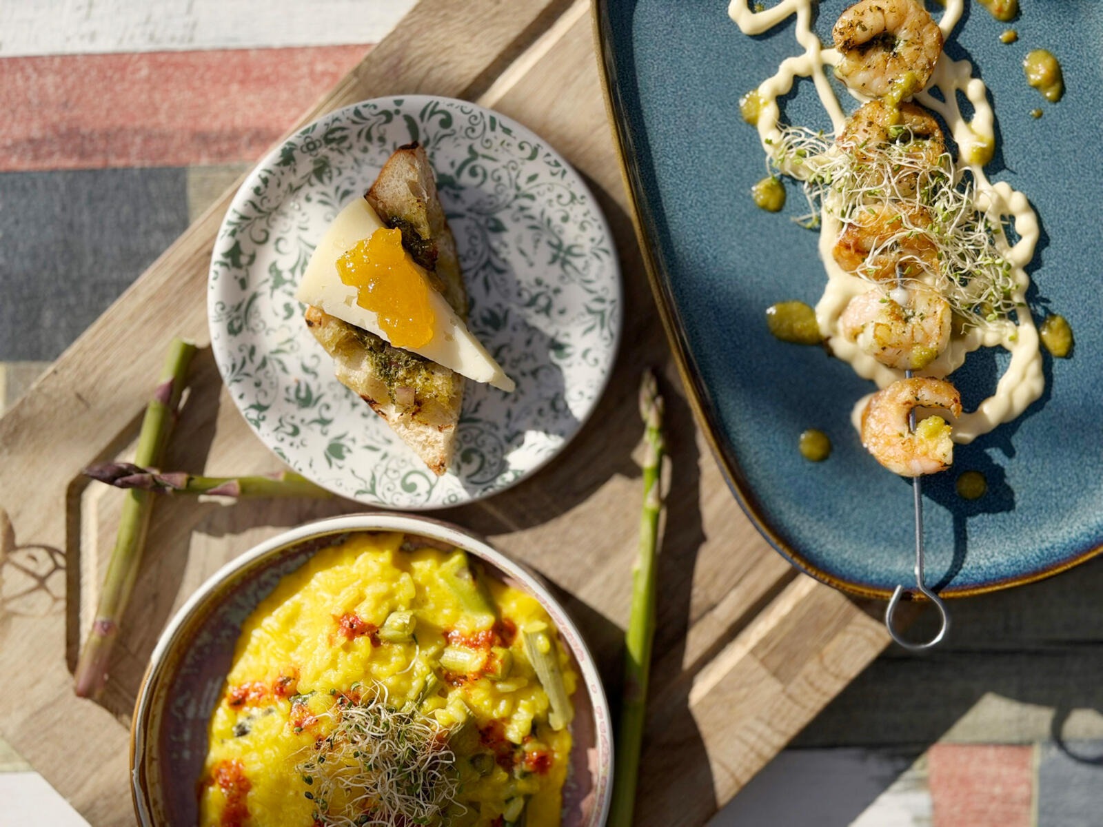 Tre läckra rätter: gul risotto, smörgåsbit med ost och frukt, samt räkrätt på en blå tallrik.