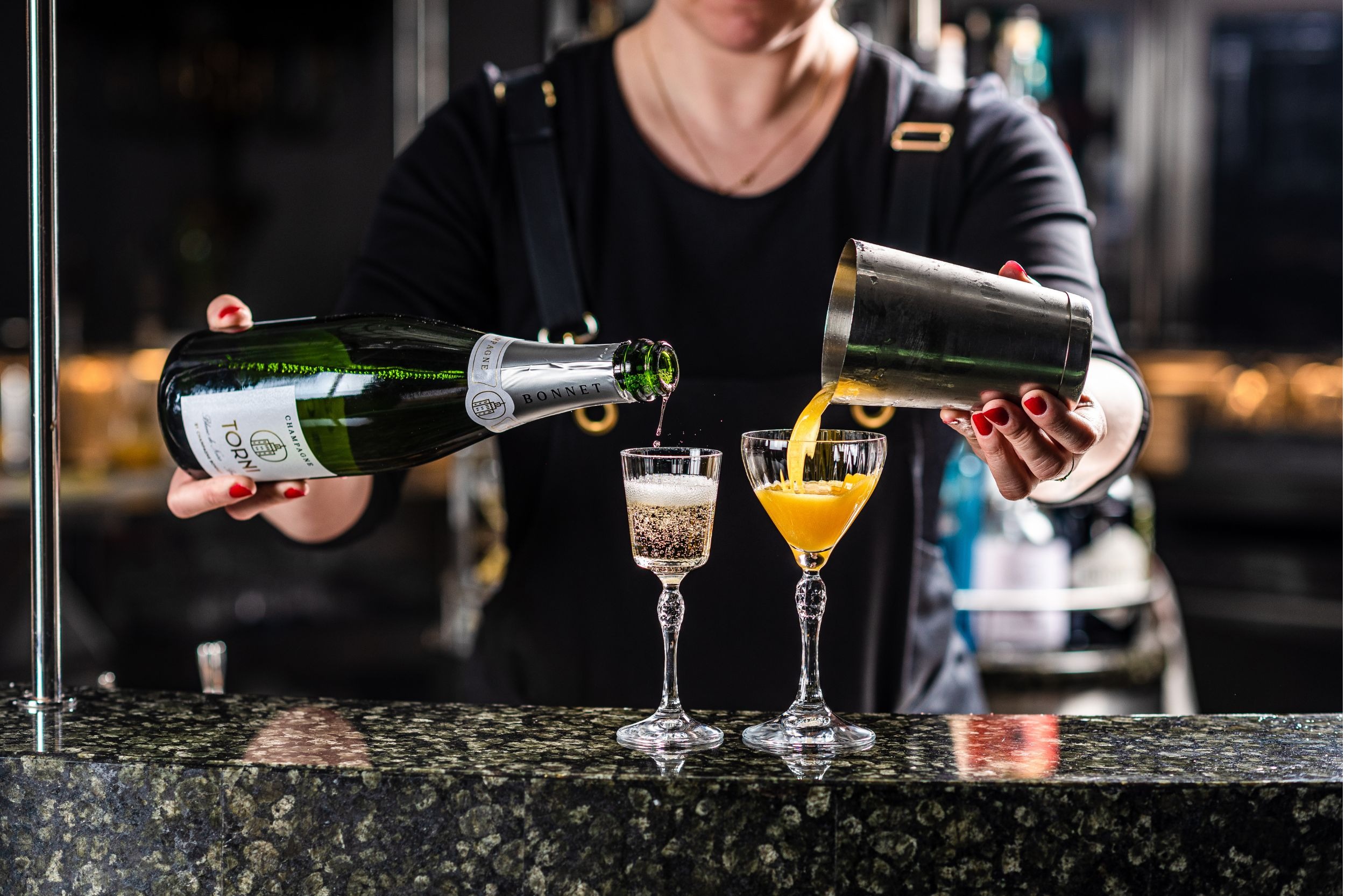 Baarimestari valmistaa samppanja-cocktaileja, kaataen samppanjaa yhteen lasiin ja appelsiinimehua toiseen.