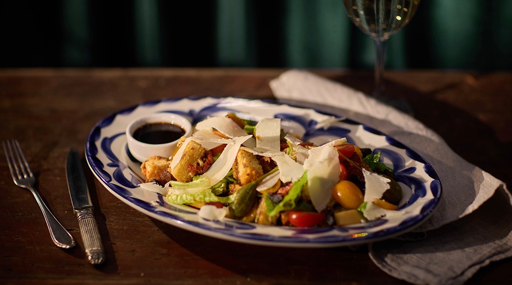 Sinise äärega taldrik itaalia pastaroaga, mille peal on parmesaanjuust ja värvilised köögiviljad, serveeritud väikese dipikastmega.