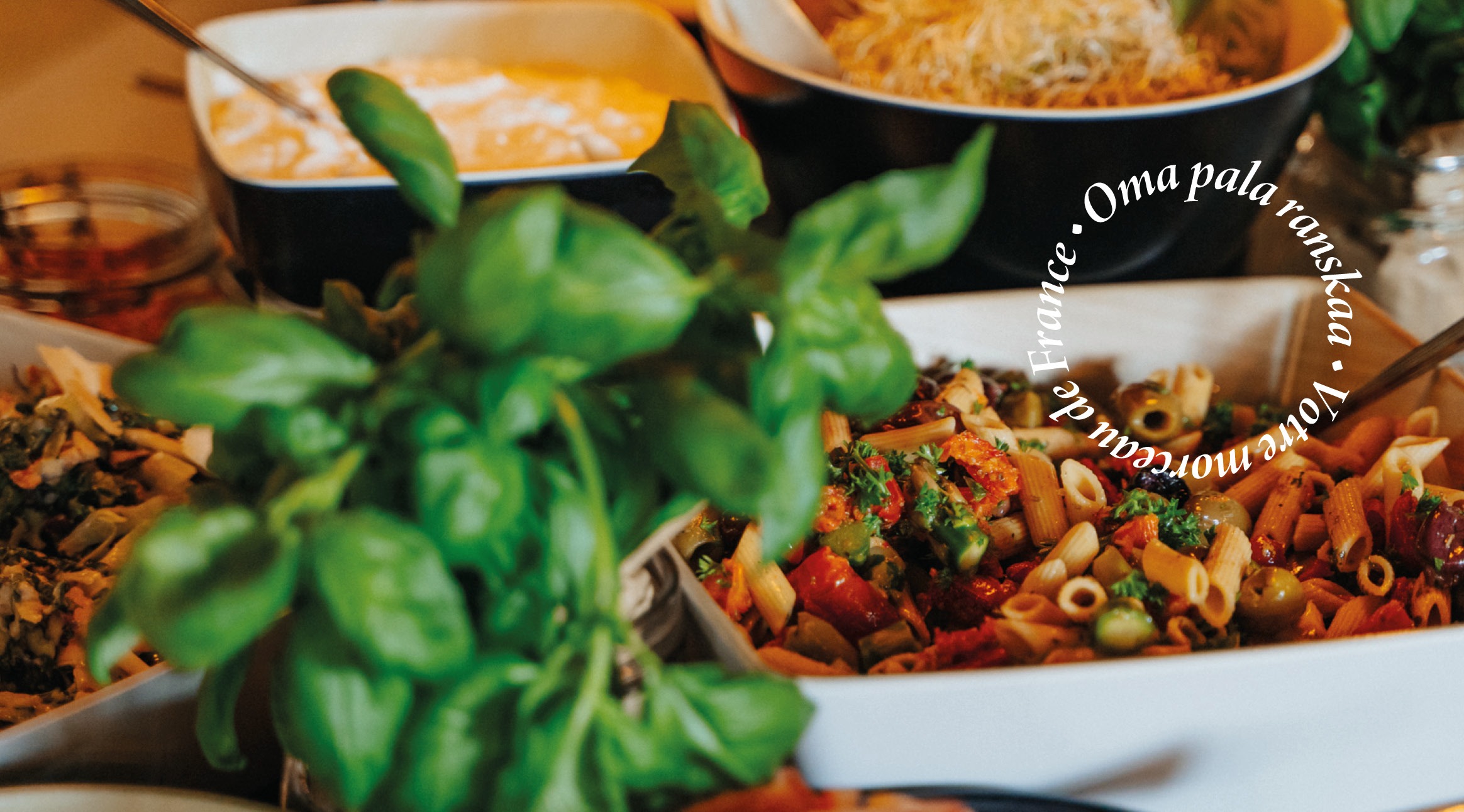 Buffetpöytä, jossa pastasalaattia, keitto ja tuoreita basilikanlehtiä etualalla.