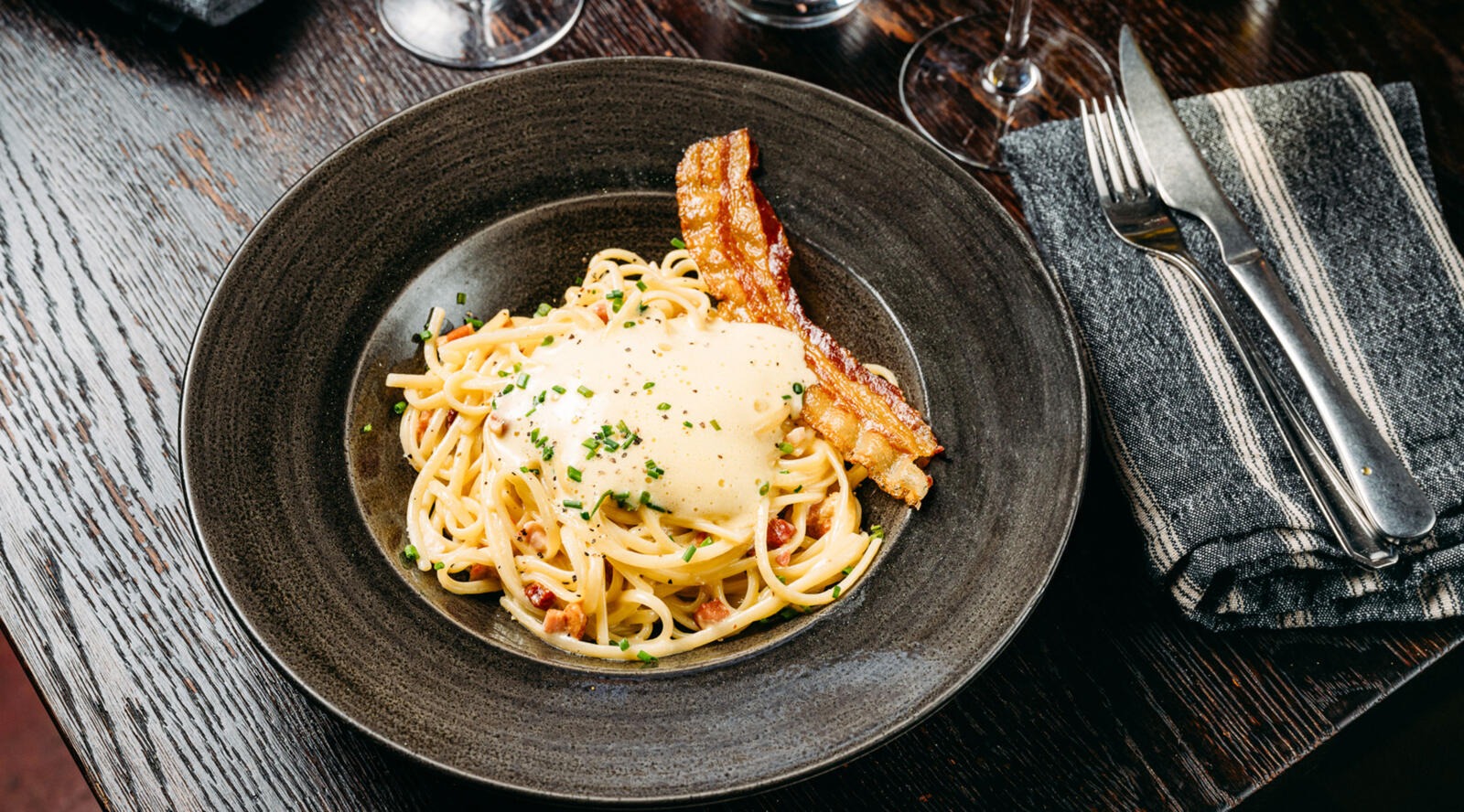 Lautasella spagettia kermakastikkeella, koristeltu paistettua pekonia ja tuoretta ruohosipulia.