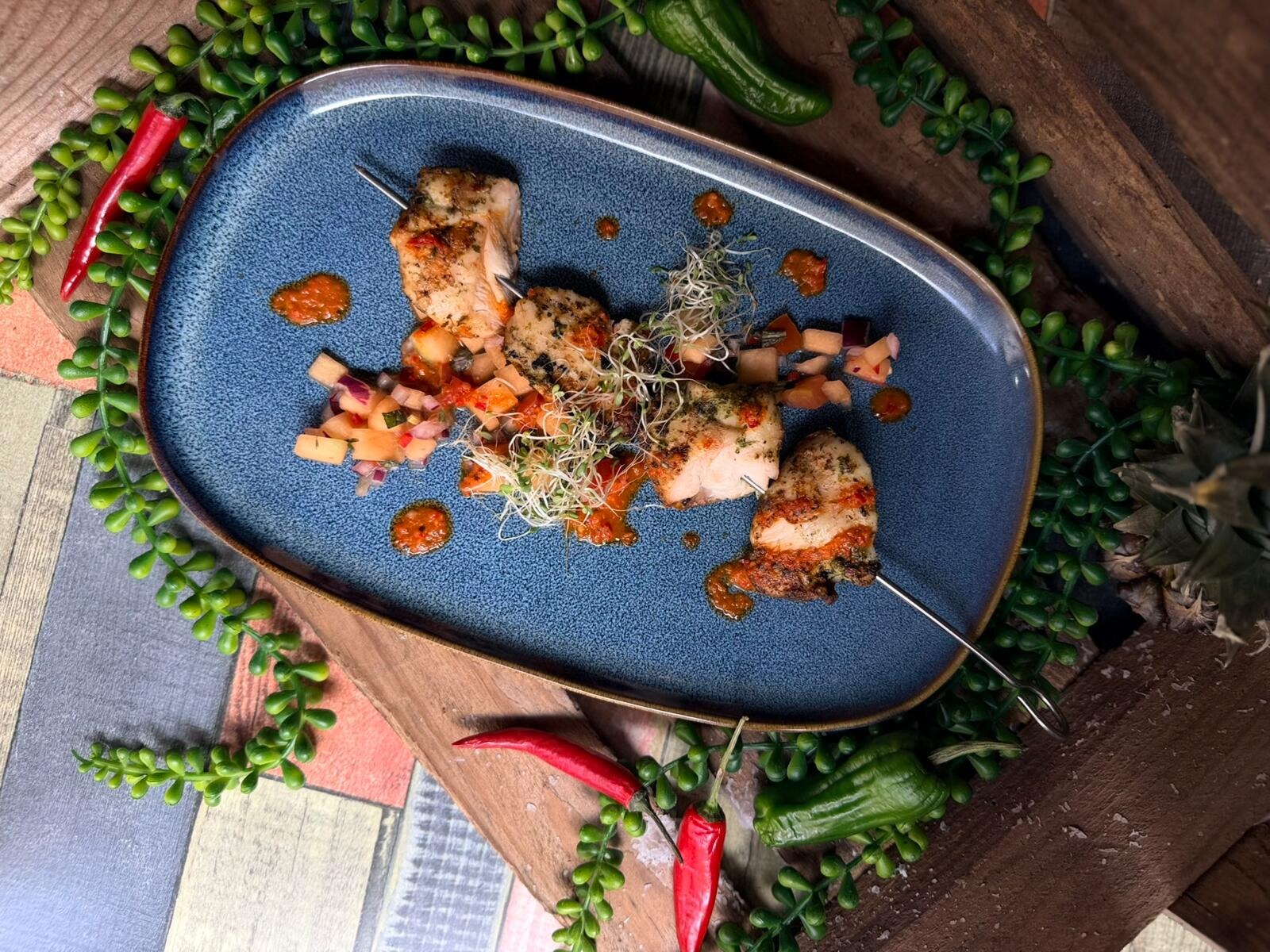 Grilled chicken skewers on a blue plate garnished with sprouts, vegetables and sauce.