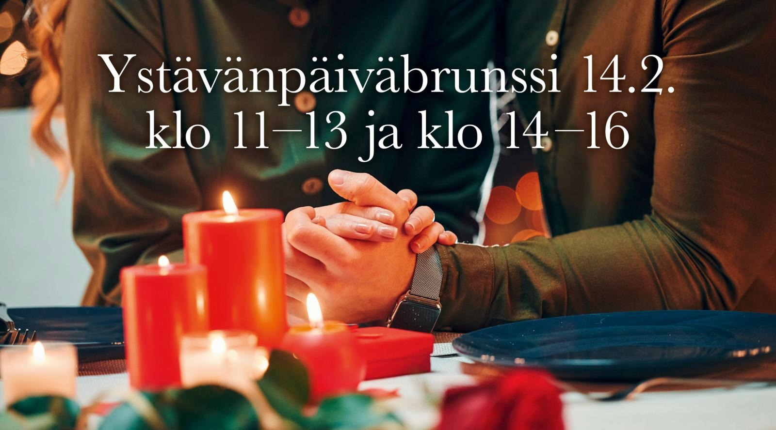 Pariskunta pitelee toisiaan kädestä kynttilöillä ja ruusuilla koristellulla ruokapöydällä.