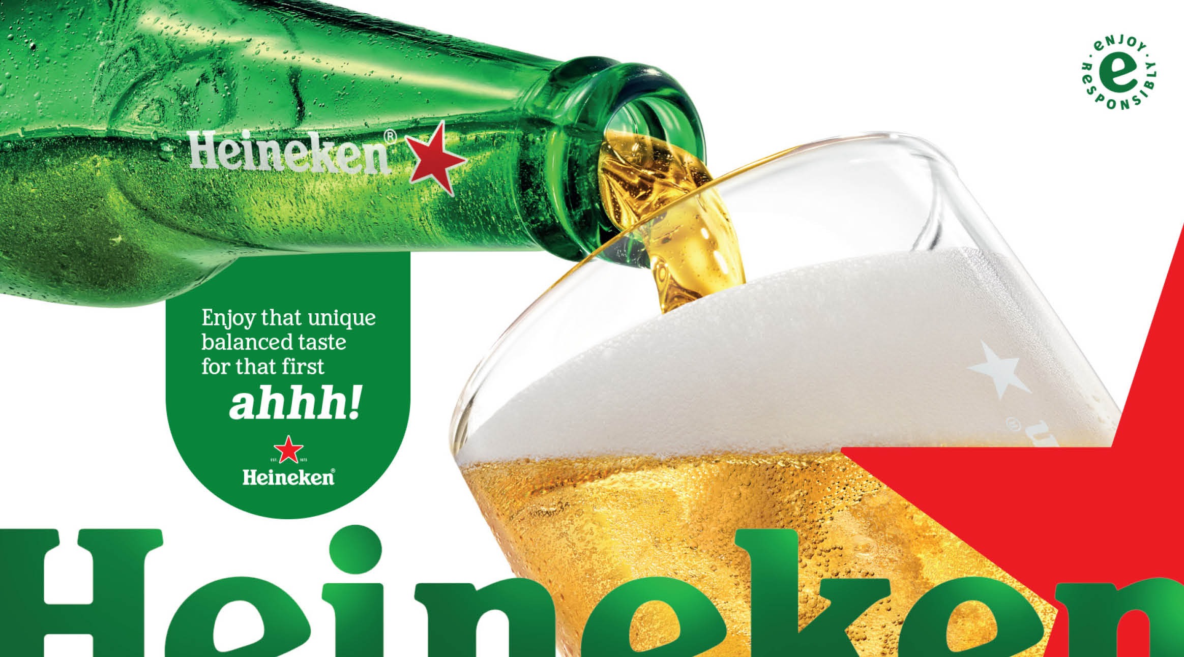 Beer pouring from a cold green Heineken bottle into a glass with pale foaming beer. Droplets on the bottle surface.