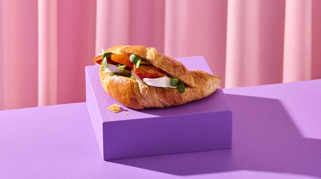 Voisarvi, jonka välissä on mozzarellaa, tomaattia ja vihreitä versoja, violetin korokkeen päällä vaaleanpunaista verhoa vasten.