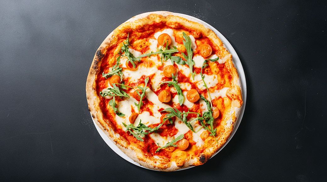 Pizza mozzarellalla, tomaateilla ja rucolalla mustalla pöydällä.