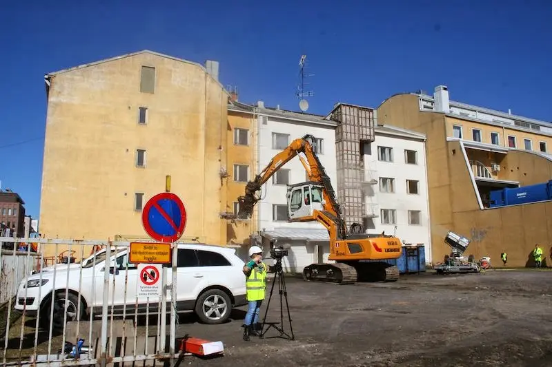Rakennusta puretaan isoilla koneilla. Etualalla insinööri tekemässä mittauksia.