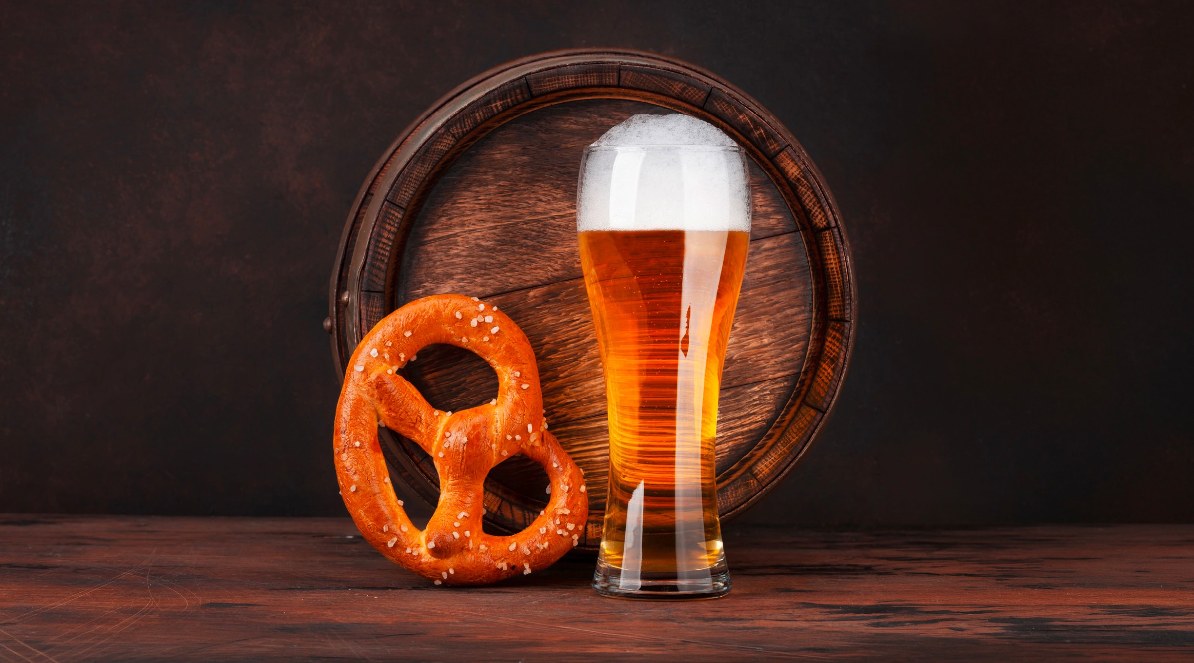 Tuopillinen olutta ja suolapretzel puisella alustalla tumman pöydän päällä.
