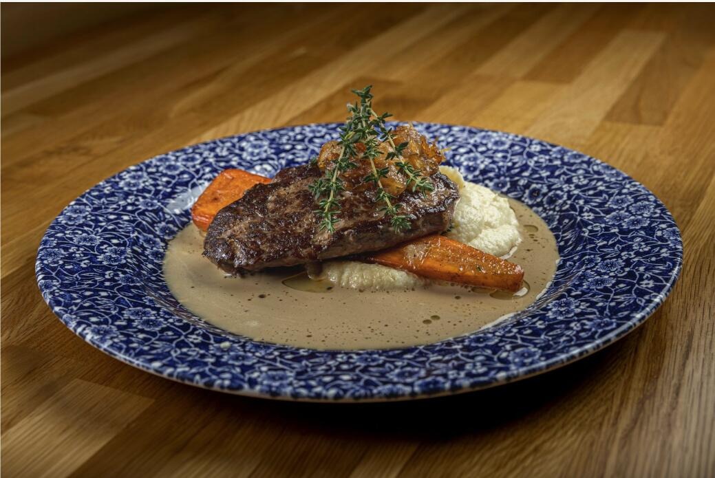 Köttbit, morötter och morotspuré på ett blåvitt fat med brun sås, garnerad med färsk timjan.