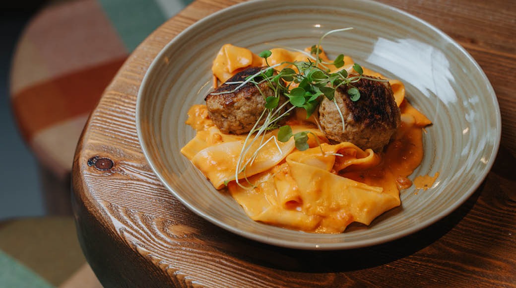 En portion pasta med köttbullar och mikroskott på en keramisk tallrik på ett träunderlag.
