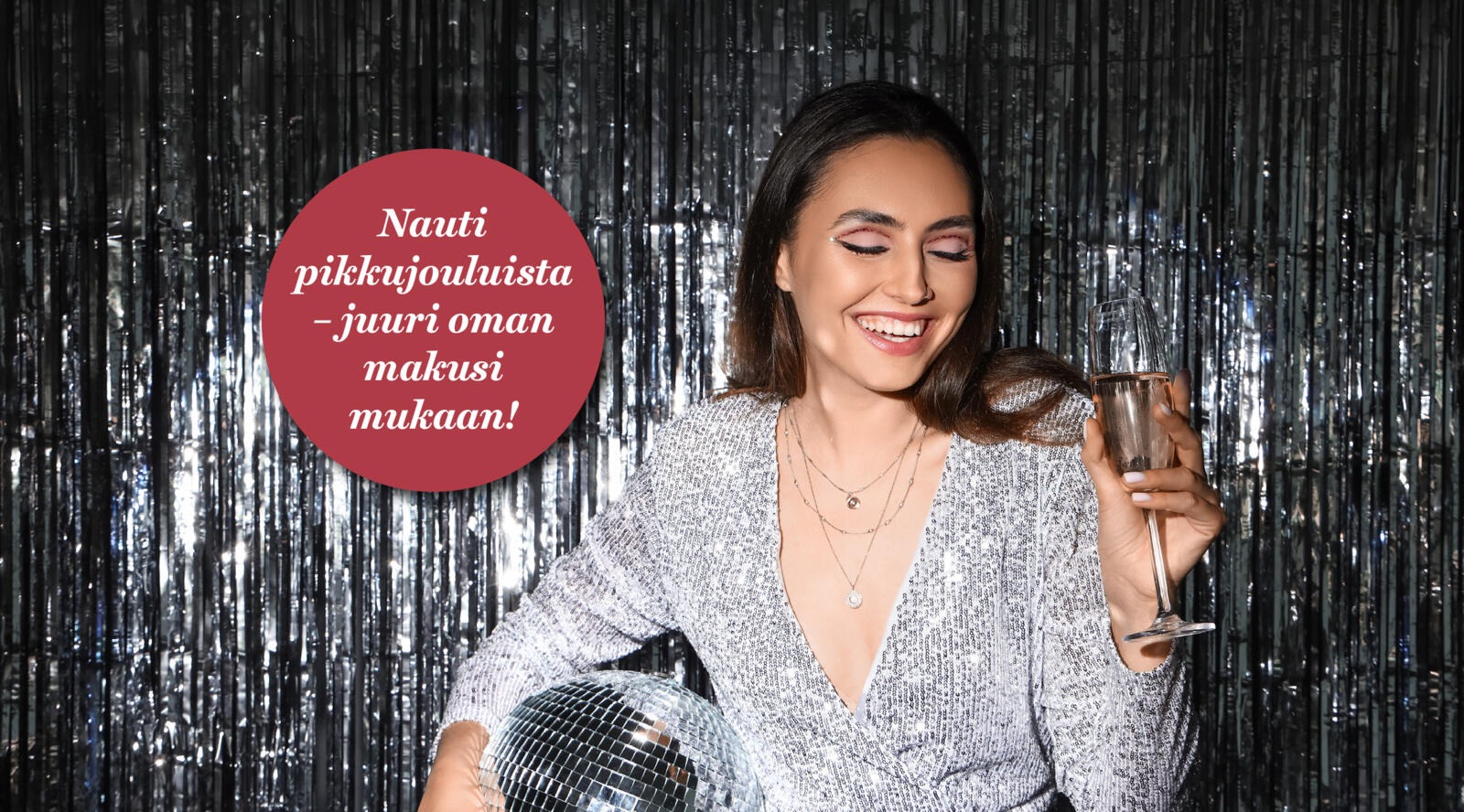 Henkilö hopeanvärisen metalliverhoilman edessä pitää discopalloa ja kuohuviinilasia.