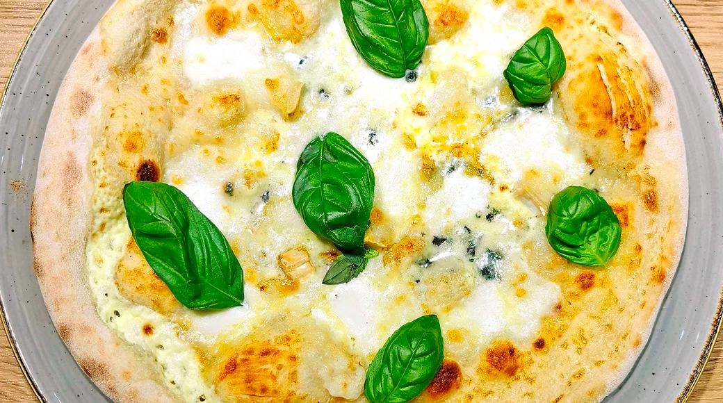 Quattro formaggi -pizza koristeltuna tuoreilla basilikan lehdillä, tarjoiltuna harmaalla lautasella.