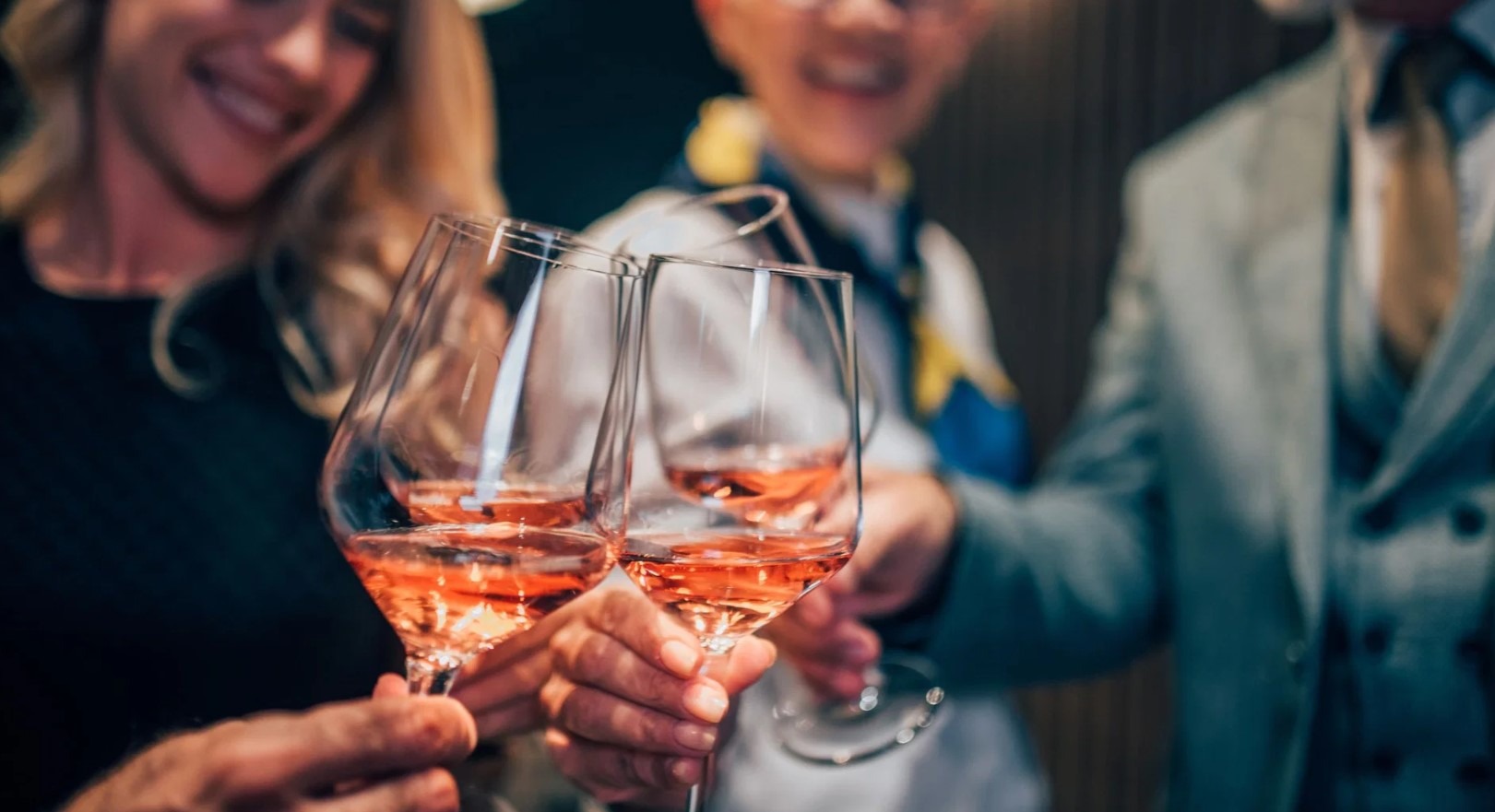 Lähikuva viinilaseista, joissa on kuohuvaa roseeviiniä, kun ihmiset kilistelevät juhlatilaisuudessa.