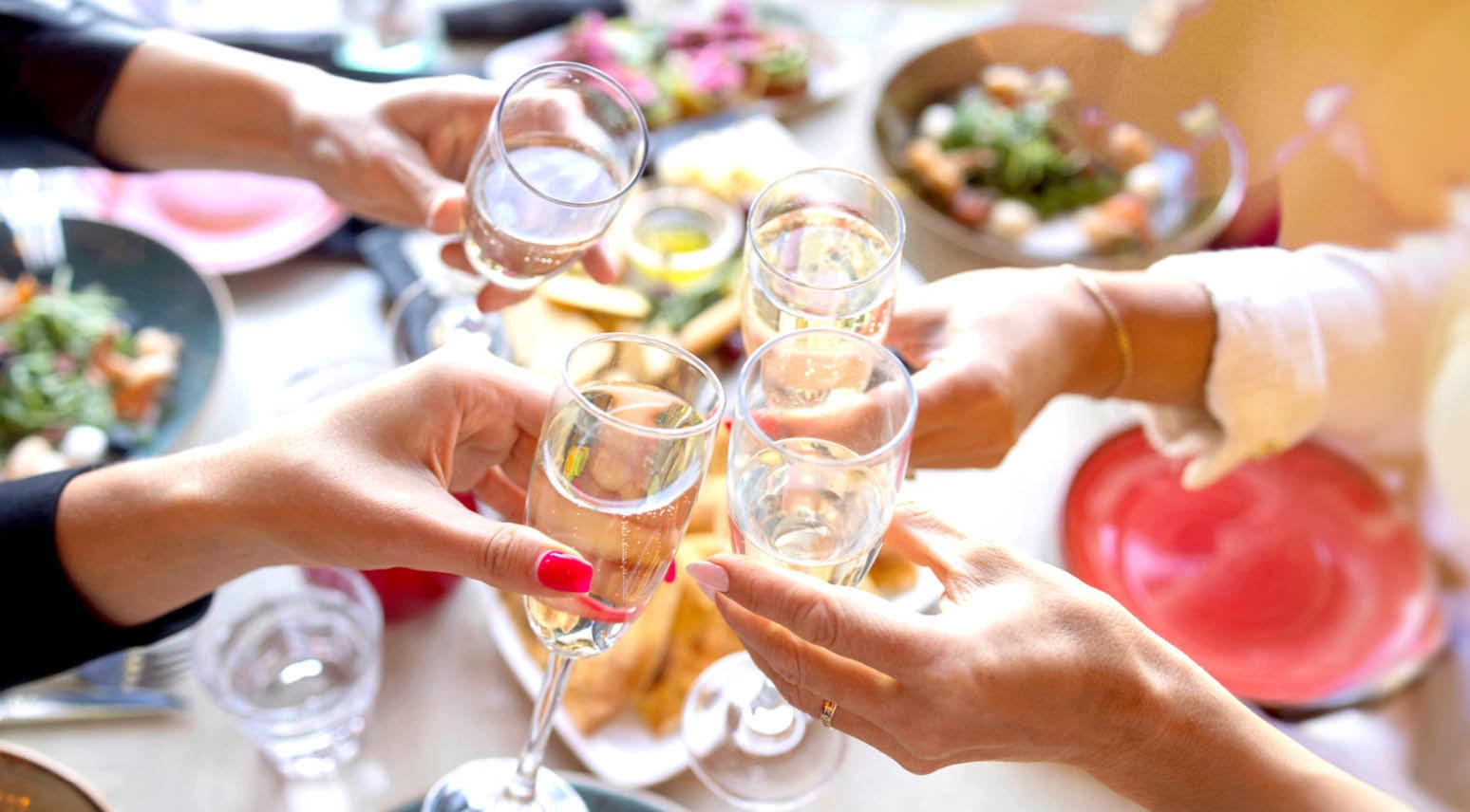 Käed tõstavad šampanjaklaase piduliku eine ajal, laual on näha salateid ja toidunõusid.