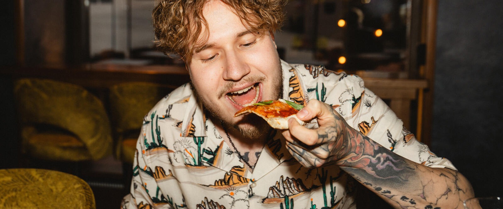 Person eating pizza in restaurant interior seating area with yellow sofa.
