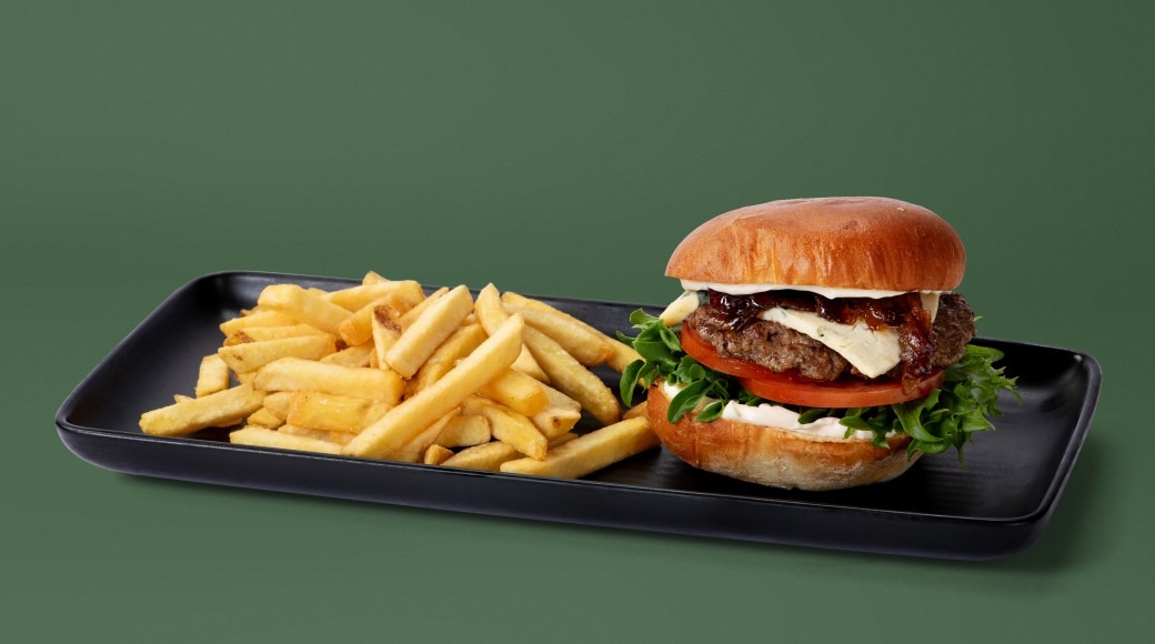 Black serving tray with burger and french fries against green background.