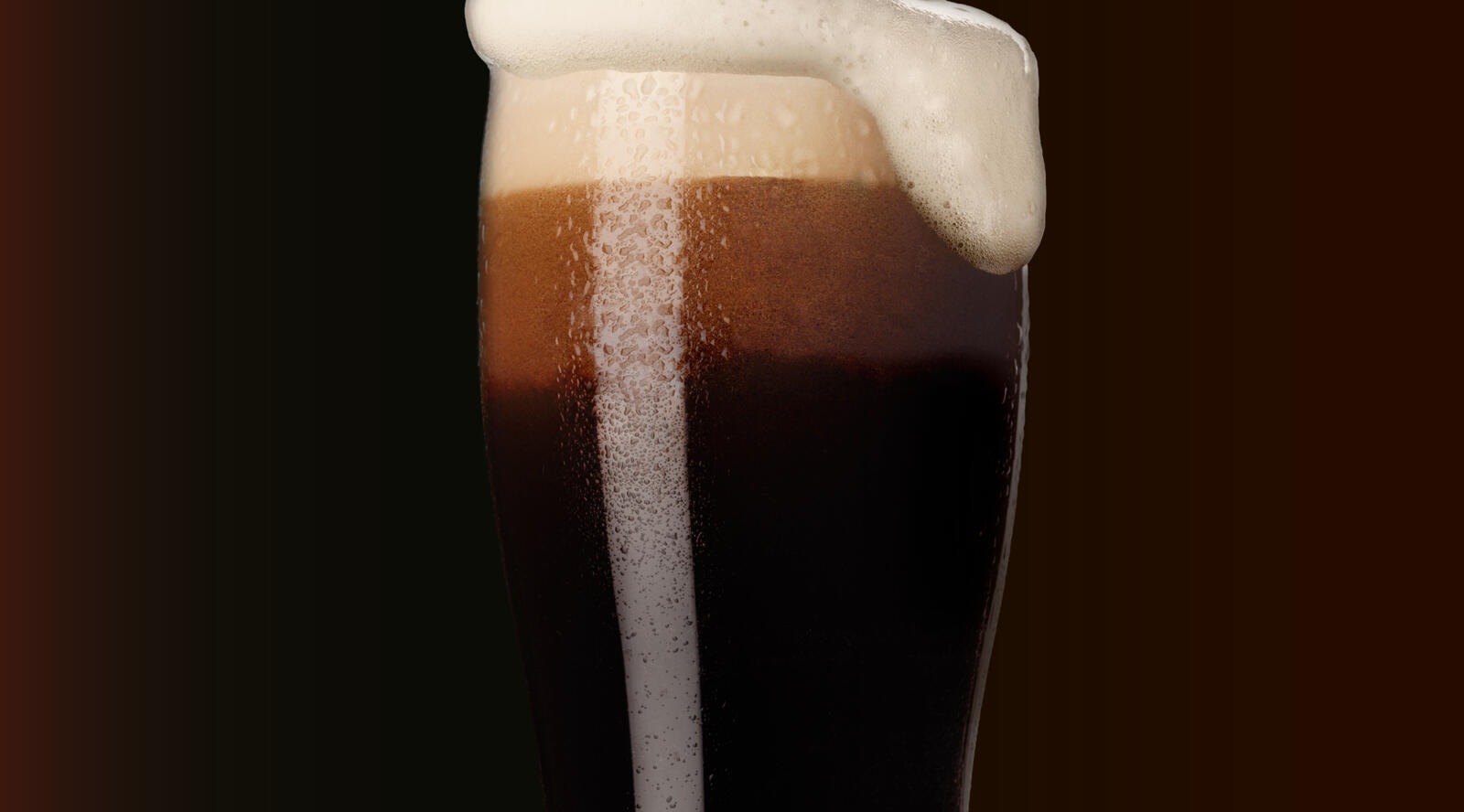 Glas med mörk öl och rikligt skum mot en mörk bakgrund.