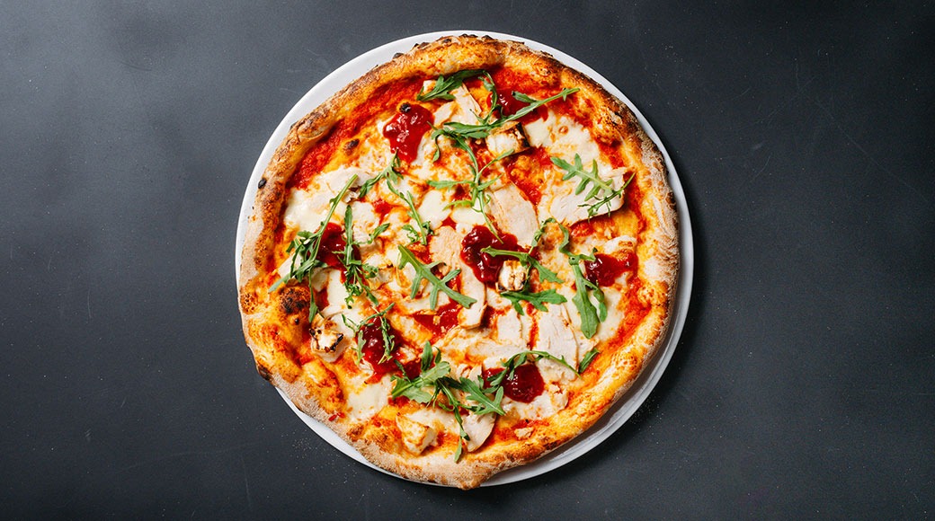 Pizza valkoisella lautasella tummanharmaan tason päällä.