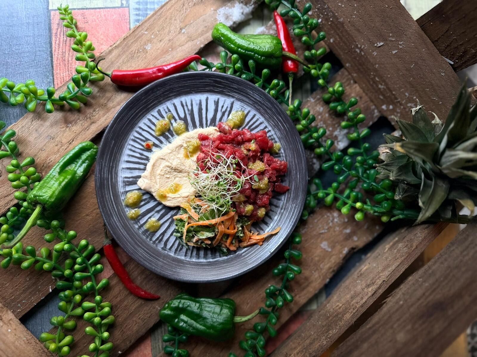 Plate with hummus, red and green chilies, and fresh vegetables on wooden board.