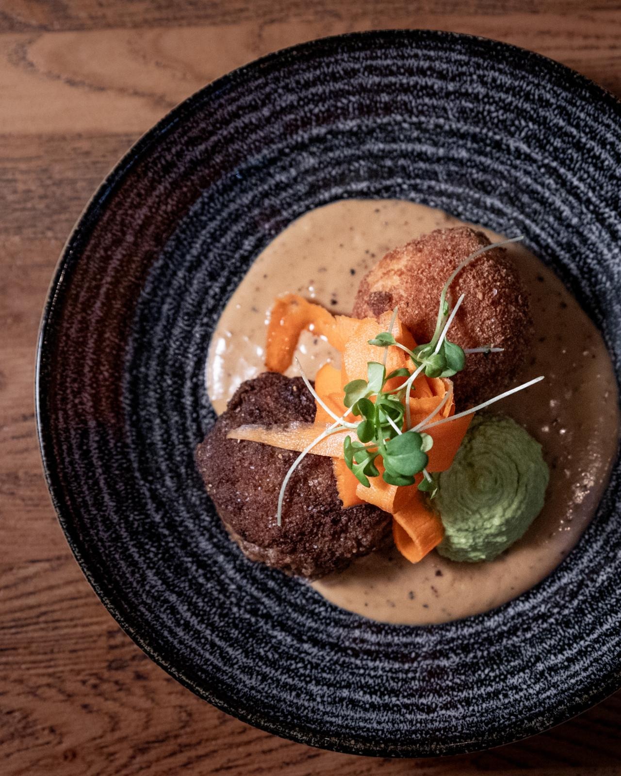 Lautasella tarjoiltu annos, jossa on karitsan Wallenberg-pihvi, konjakki - pippurikastiketta, perunakroketti, hernepyreetä ja pikkelöityä porkkanaa.