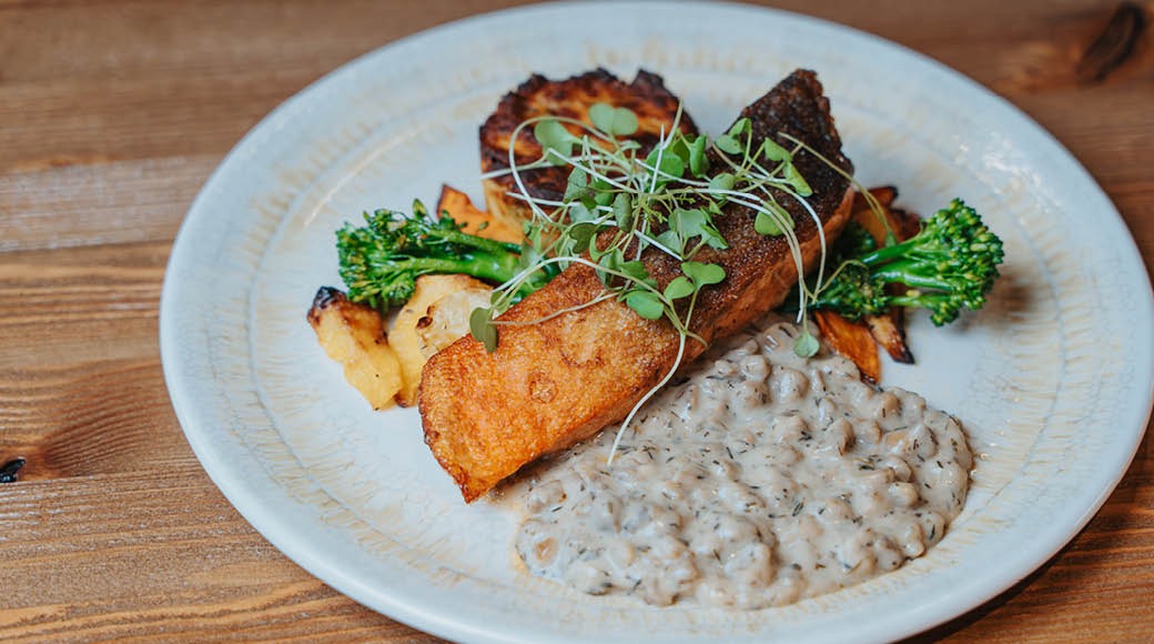 Annos vaalealla lautasella: rapeapintainen kalafile, paahdettua perunaa, parsakaalia ja kermaista kastiketta, koristeena mikroyrttejä.