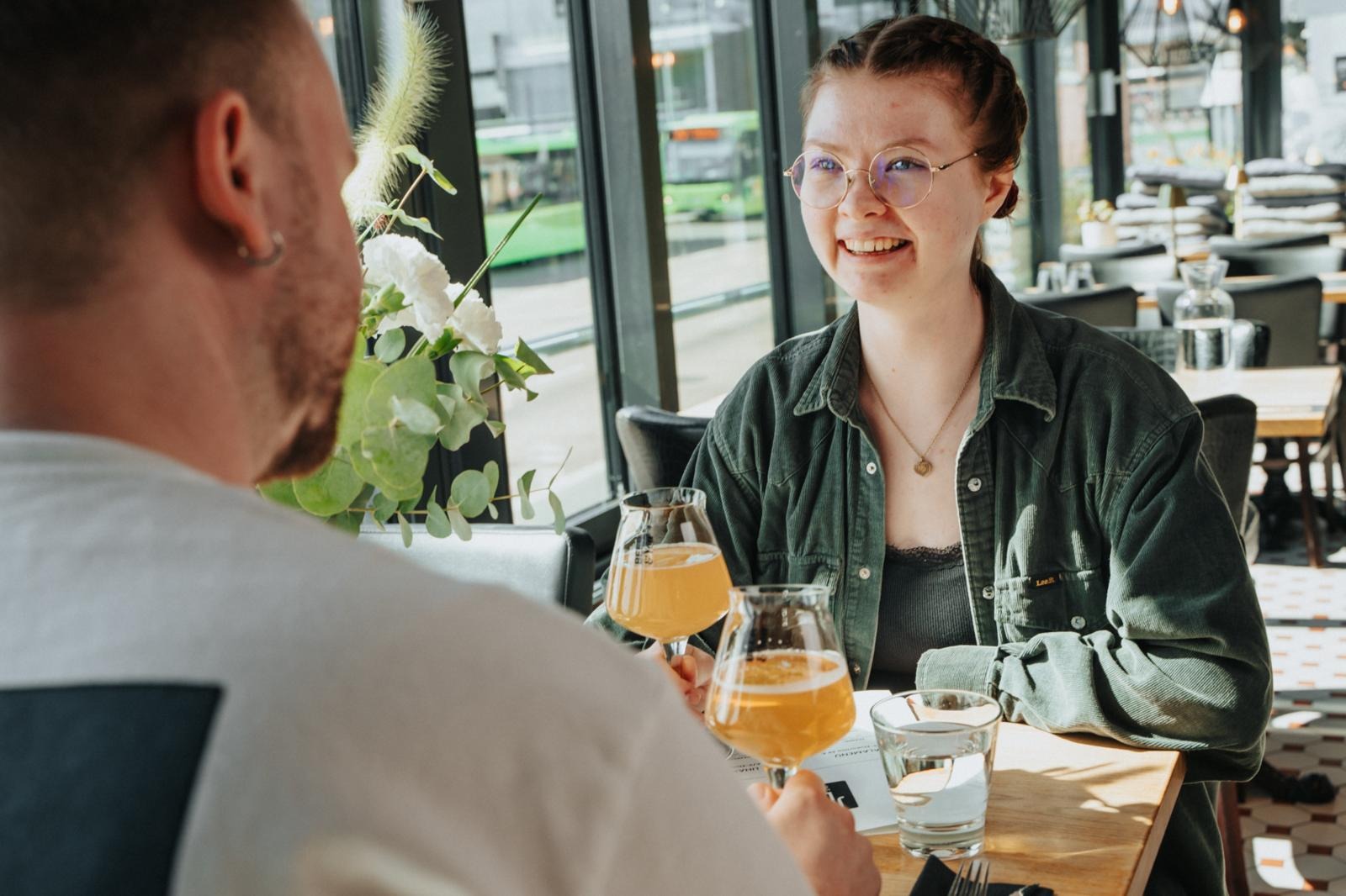 Two people sit at a restaurant table with drinks. The floor is level and there is space between tables.